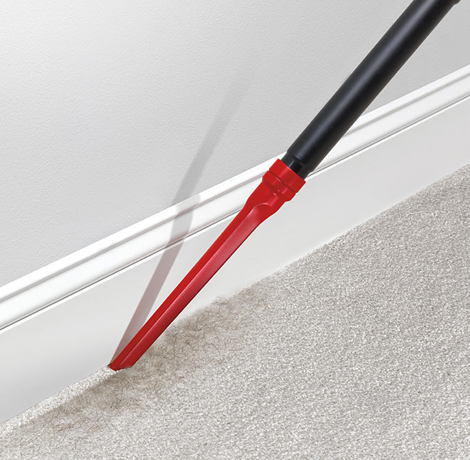 Close up of windtunnel vacuum cleaner's crevice tool cleaning along the baseboard on a carpeted floor.