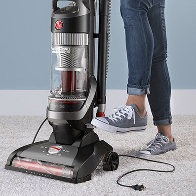 Hoover windtunnel vacuum cleaner being used on a carpet, featuring 25ft automatic cord rewind, shown by a person pressing the pedal with their foot for easy and efficient clean up