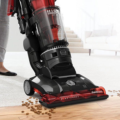 A person vacuuming a hard floor with the Hoover windtunnel high performance pet vacuum cleaner in action, effectively picking up scattered pet food