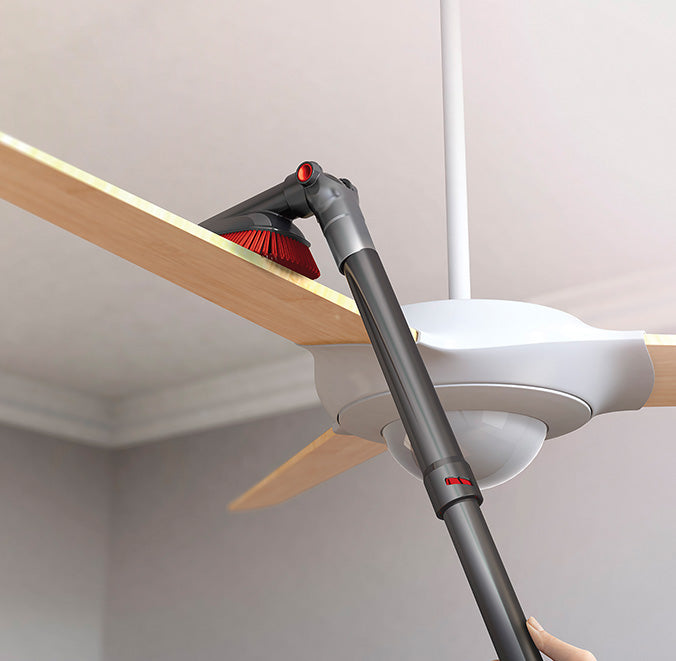 A vacuum cleaner extended length crevice tool attachment being used to clean a ceiling fan blade, demonstrating its capability to reach high and difficult areas for effective dust removal