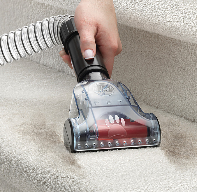 Close up of hand using the Hoover pet turbo tool, specifically designed for pet hair removal, to vacuum hair from a carpeted staircase.