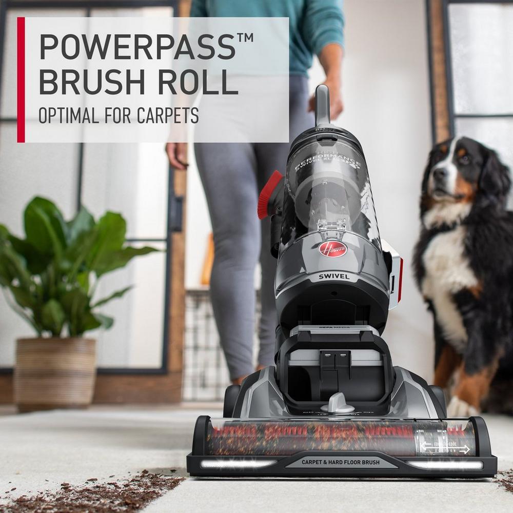 Close up of a hoover vacuum cleaner in action, easily vacuuming dirt and debris from a light colored carpet because of the powerpass brush roll
