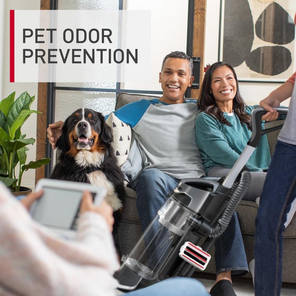 A happy family sitting on a sofa with their dog, highlighting the Hoover vacuum cleaner's pet odor prevention feature