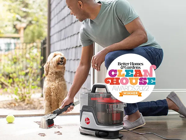 Man cleaning paw prints off of white carpet with dog and ball in background