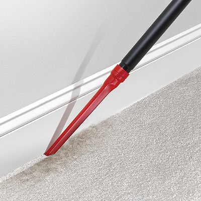 Close up of the Hoover crevice tool attachment being used to clean along the edge of a carpet and baseboard highlighting it's ability to reach narrow and tight spaces