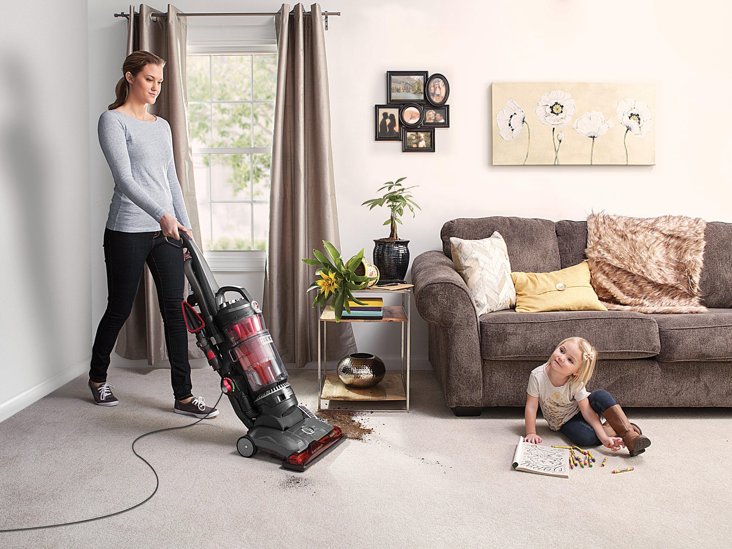 A woman is vacuuming a pile of dirt from a spilled plant pot off a light colored carpet in a living room with the hoover windtunnel high performance pet vacuum cleaner.