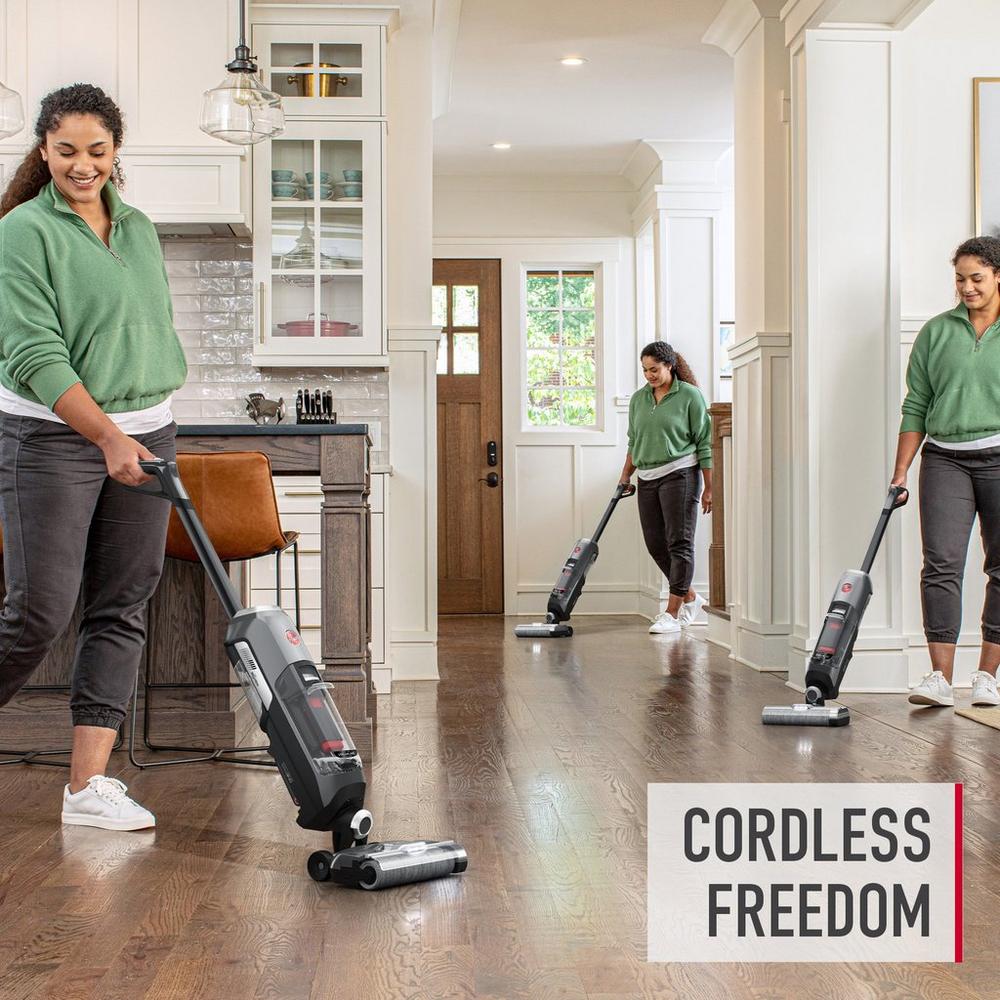 Woman enjoys using a cordless vacuum cleaner in a spacious, modern kitchen and hallway, promoting the convenience of cordless freedom.  