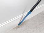 Using a Hoover crevice tool to clean along the baseboard and carpet edge, highlighting precise and thorough cleaning in tight spaces 