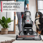 Close up of a hoover vacuum cleaner in action, easily vacuuming dirt and debris from a light colored carpet because of the powerpass brush roll